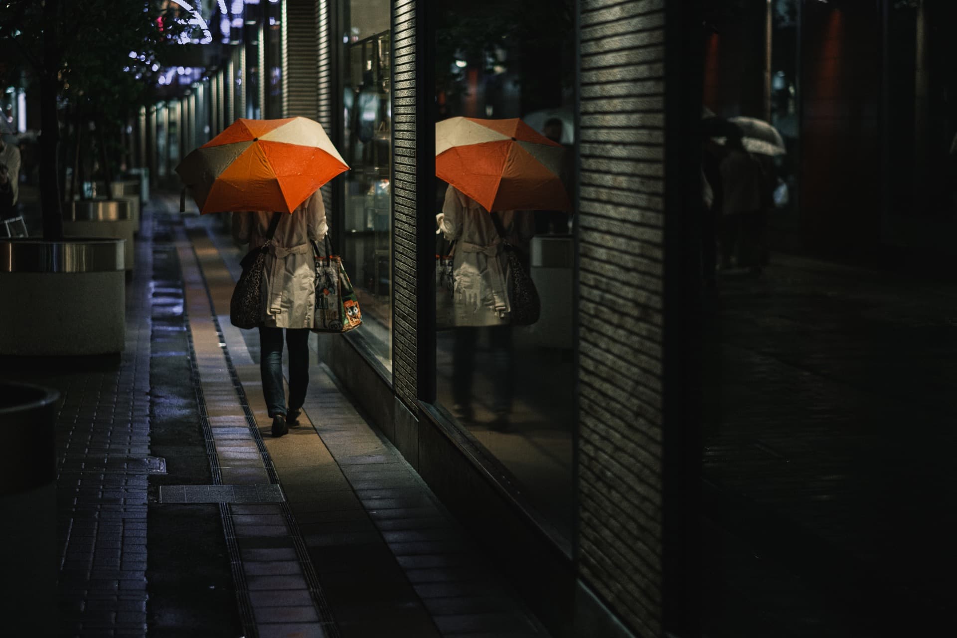 夜の街を傘と共に歩く女性